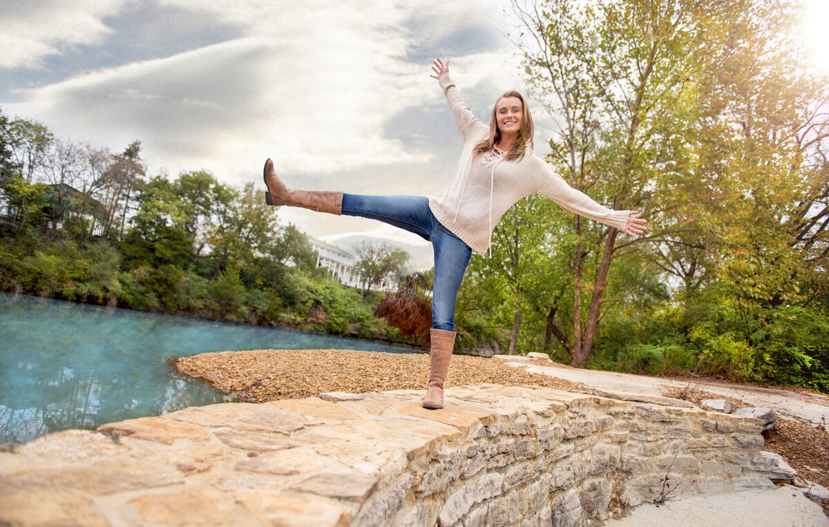 Woman balancing playfully on stones by a river
